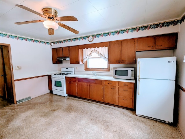 kitchen featuring brown cabinetry, white appliances, light countertops, and a sink