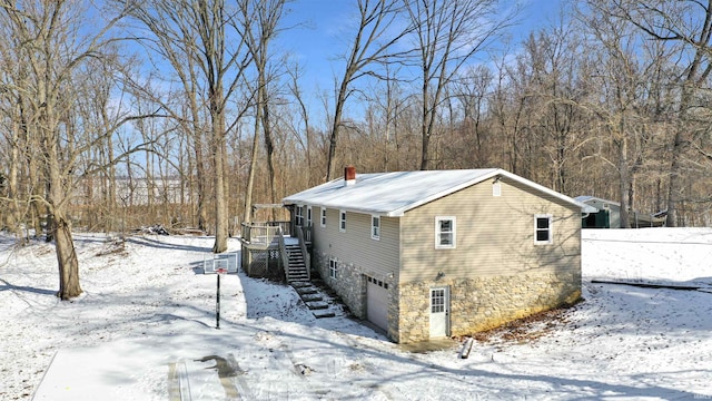 snow covered property with a garage, a chimney, and stairs