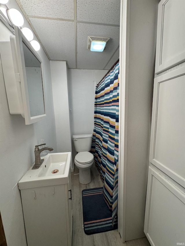 bathroom with curtained shower, a drop ceiling, toilet, wood finished floors, and vanity