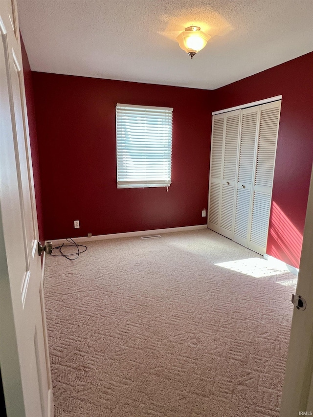 unfurnished bedroom with carpet, a textured ceiling, baseboards, and a closet