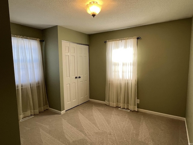 unfurnished bedroom with a closet, light carpet, a textured ceiling, and baseboards