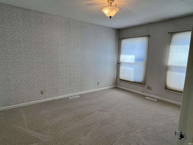 empty room with carpet, visible vents, a textured ceiling, and wallpapered walls