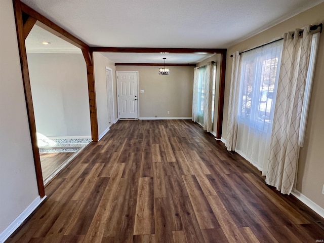 unfurnished room featuring a notable chandelier, dark wood finished floors, and baseboards