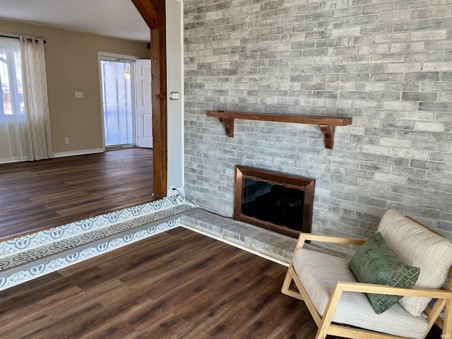 unfurnished living room with dark wood-type flooring, a brick fireplace, and baseboards