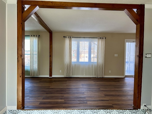 unfurnished room featuring beamed ceiling, dark wood-style flooring, and baseboards