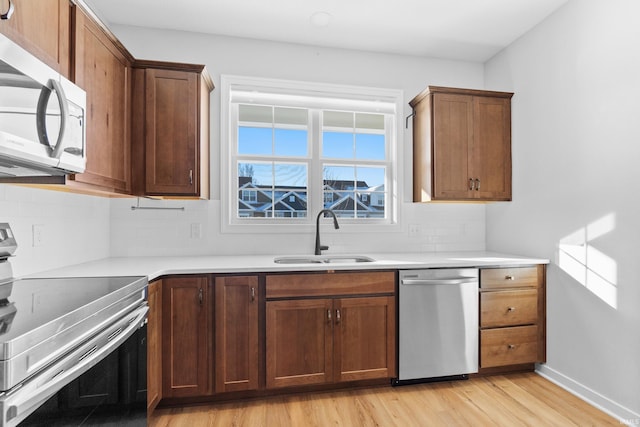 kitchen featuring stainless steel appliances, light countertops, light wood-style flooring, decorative backsplash, and a sink