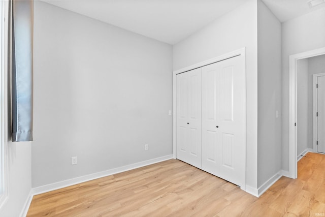 unfurnished bedroom featuring light wood-style floors, baseboards, and a closet