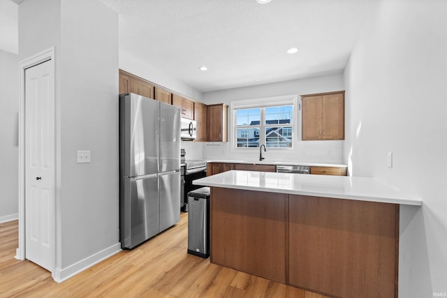 kitchen with a peninsula, brown cabinetry, stainless steel appliances, and light countertops