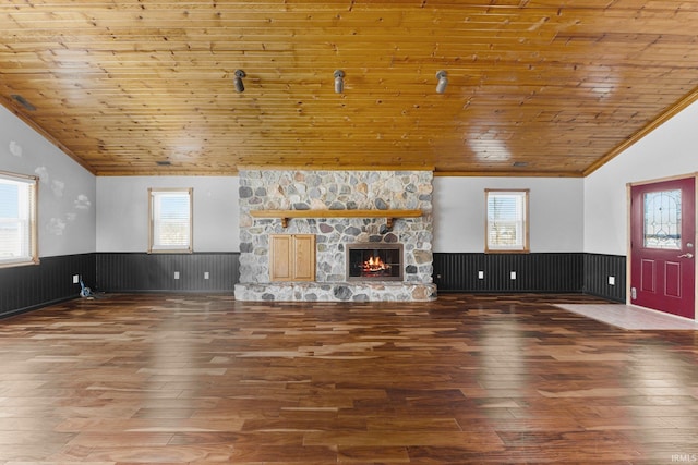 unfurnished living room featuring lofted ceiling, wood ceiling, wainscoting, a stone fireplace, and wood finished floors