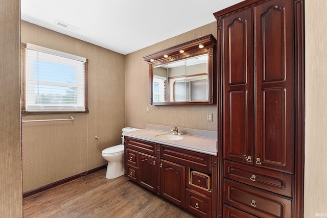 bathroom with toilet, wood finished floors, vanity, visible vents, and baseboards