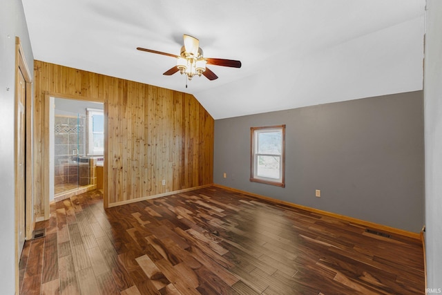 spare room featuring wooden walls, baseboards, a ceiling fan, dark wood-style floors, and vaulted ceiling