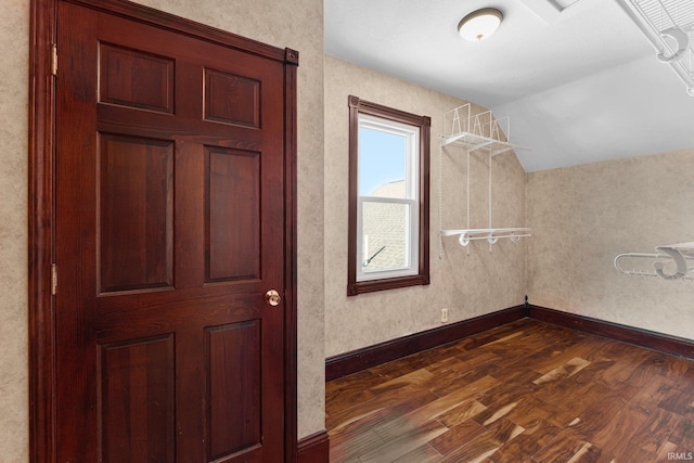 interior space with baseboards, vaulted ceiling, and dark wood-style flooring