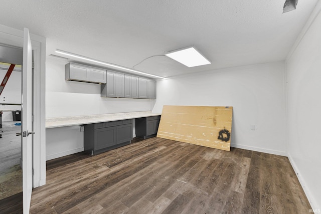 unfurnished office featuring dark wood-style floors, a textured ceiling, built in study area, and baseboards