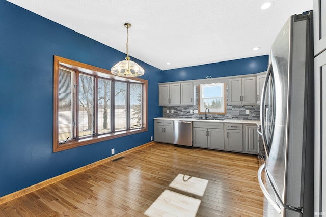 kitchen with appliances with stainless steel finishes, decorative light fixtures, light countertops, gray cabinetry, and a sink