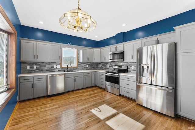 kitchen with gray cabinets, appliances with stainless steel finishes, light countertops, and decorative light fixtures