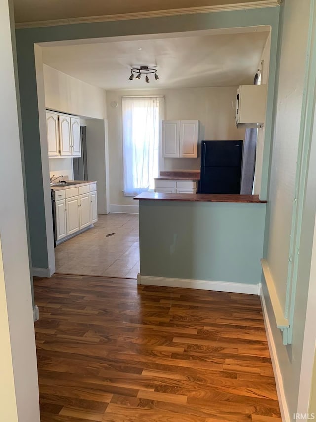 kitchen featuring dark wood finished floors, freestanding refrigerator, white cabinets, a peninsula, and baseboards