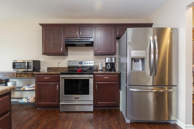 kitchen featuring under cabinet range hood, dark wood-style flooring, dark brown cabinets, appliances with stainless steel finishes, and dark stone counters