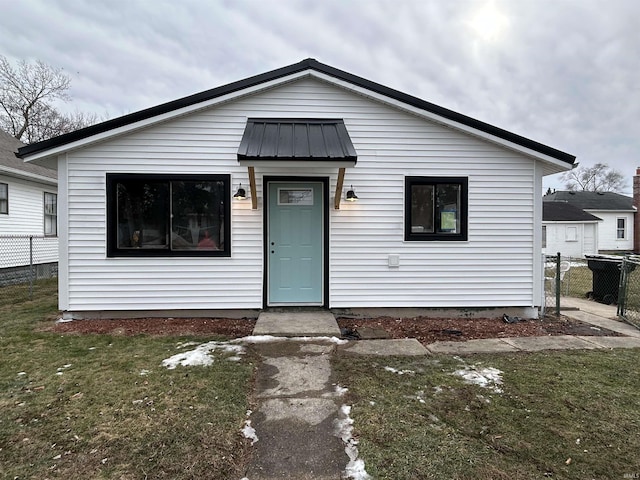 bungalow-style house with metal roof, a front lawn, and fence