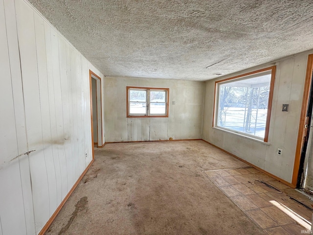 empty room with light carpet, wood walls, baseboards, and a textured ceiling