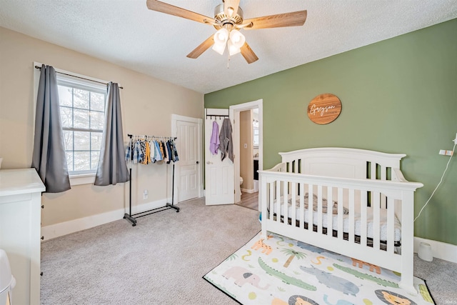 bedroom with a textured ceiling, a nursery area, baseboards, and light colored carpet