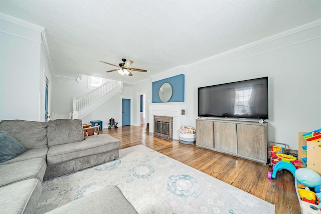 living room featuring a textured ceiling, a fireplace with flush hearth, wood finished floors, stairs, and crown molding