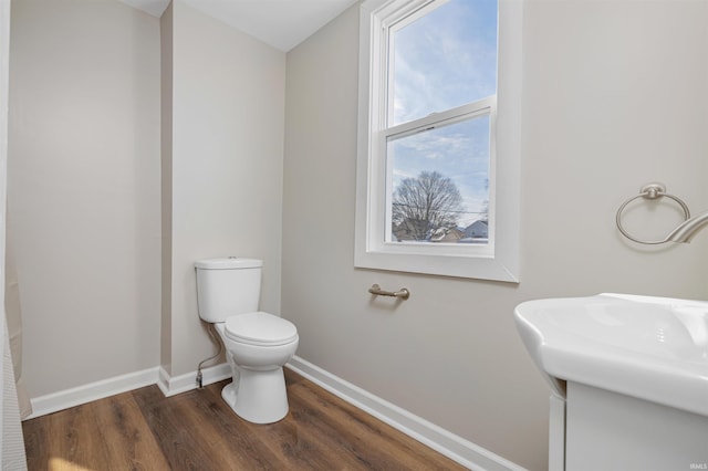 half bath with baseboards, a sink, toilet, and wood finished floors