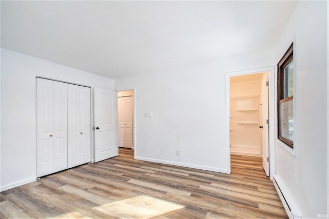 unfurnished bedroom featuring light wood finished floors, baseboards, a baseboard heating unit, and a closet