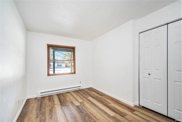 unfurnished bedroom with a baseboard radiator, a closet, baseboards, and wood finished floors