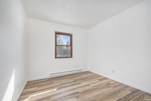 empty room with a baseboard heating unit, light wood finished floors, and baseboards