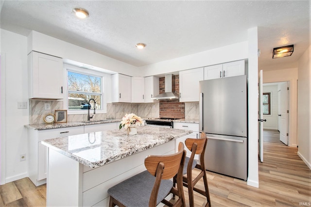 kitchen featuring white cabinets, wall chimney exhaust hood, stainless steel appliances, and a sink