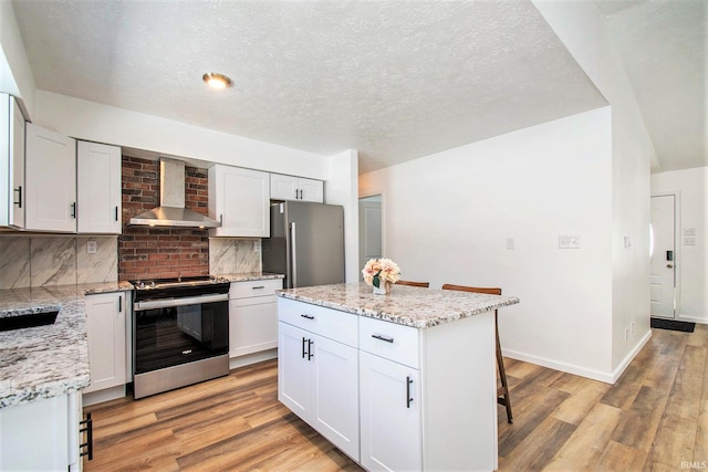 kitchen with appliances with stainless steel finishes, white cabinetry, wall chimney exhaust hood, and a kitchen bar