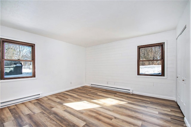 unfurnished room with baseboards, a baseboard heating unit, and wood finished floors