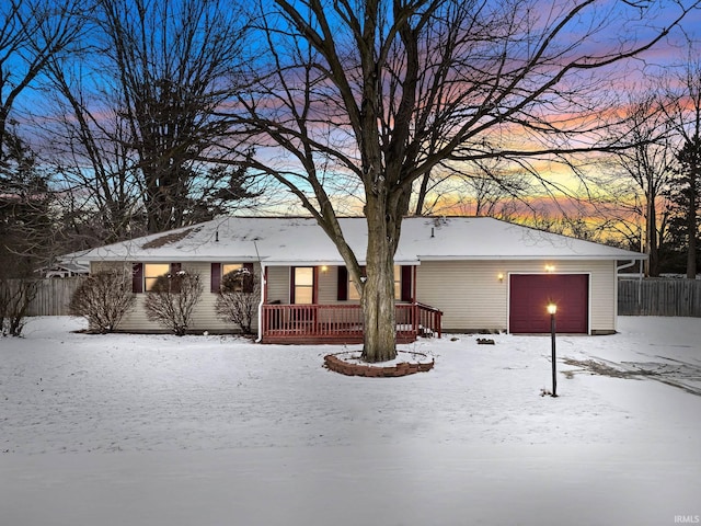 snow covered house featuring fence and an attached garage