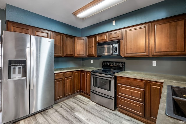 kitchen with brown cabinets, light wood-style flooring, stainless steel appliances, and a sink