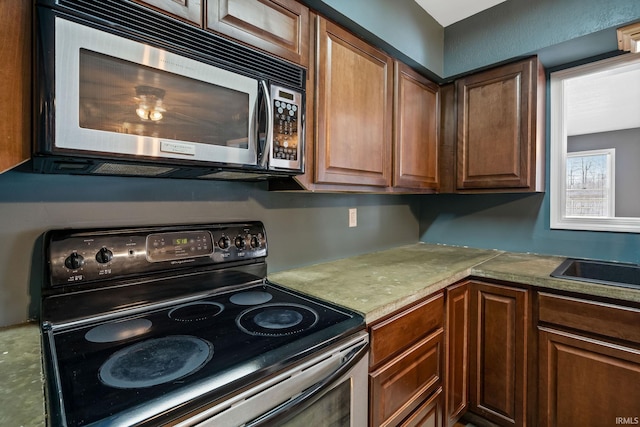 kitchen featuring electric range, a sink, light countertops, brown cabinetry, and stainless steel microwave