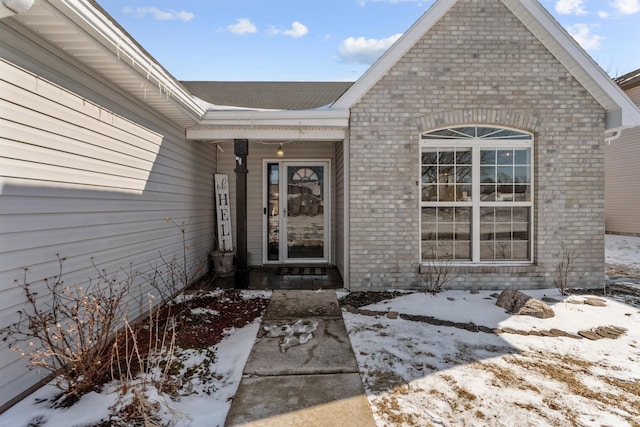 snow covered property entrance with brick siding