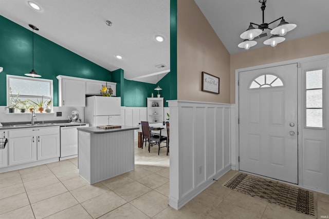 interior space with white appliances, a sink, white cabinets, vaulted ceiling, and wainscoting