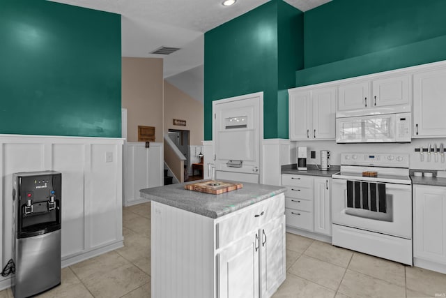 kitchen with white appliances, wainscoting, white cabinetry, and a center island