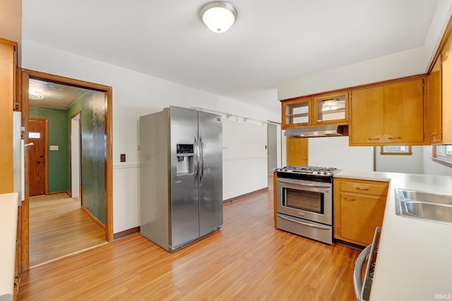 kitchen featuring brown cabinetry, light wood-style flooring, stainless steel appliances, light countertops, and under cabinet range hood