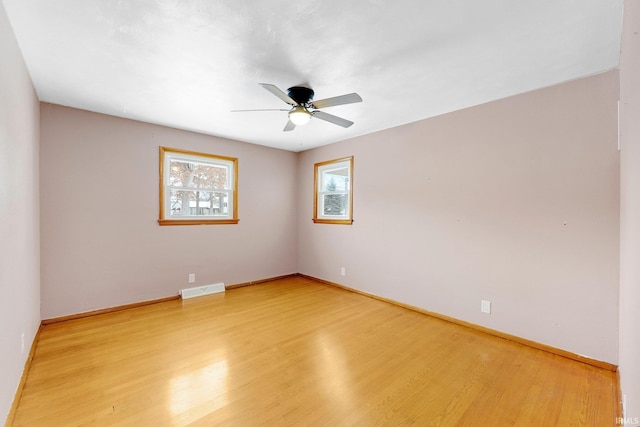 spare room featuring light wood finished floors, baseboards, visible vents, and ceiling fan