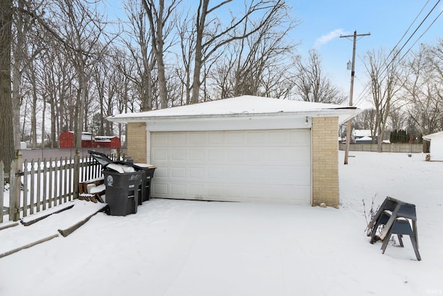 snow covered garage featuring a garage and fence