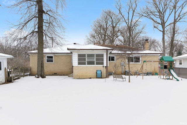 snow covered back of property with a playground, brick siding, and a chimney