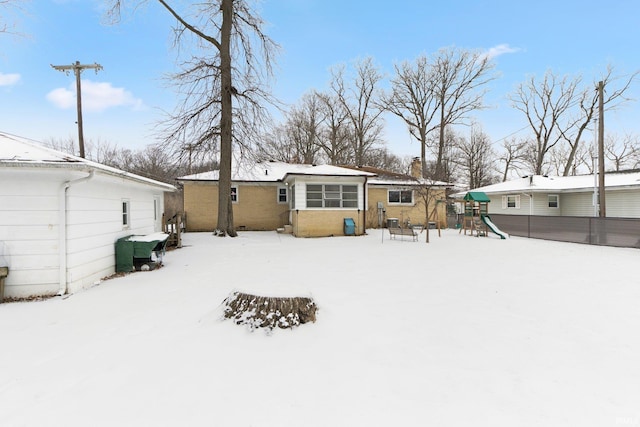 snow covered back of property featuring a chimney and a playground