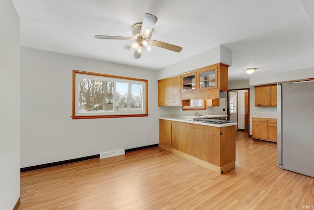 kitchen featuring visible vents, glass insert cabinets, a peninsula, stainless steel appliances, and light countertops