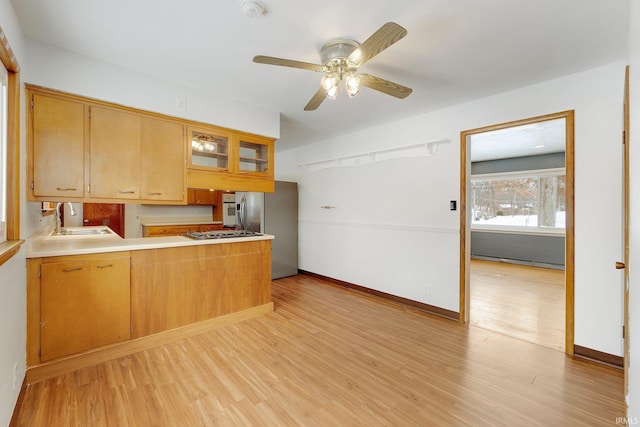 kitchen featuring light countertops, light wood-style flooring, glass insert cabinets, a sink, and a peninsula