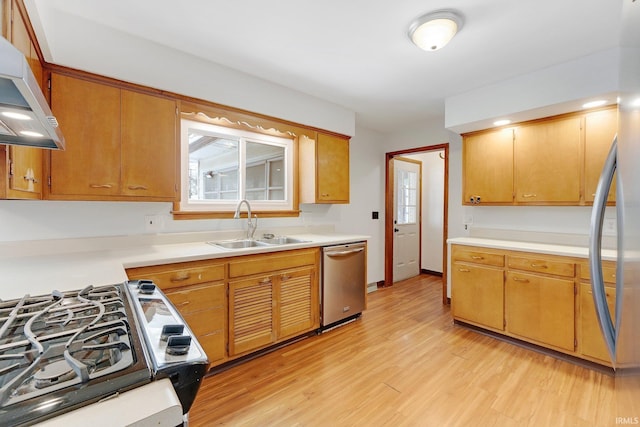 kitchen with light wood-style flooring, stainless steel appliances, a sink, light countertops, and wall chimney range hood