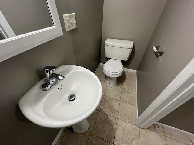 half bathroom with tile patterned flooring, baseboards, a sink, and toilet