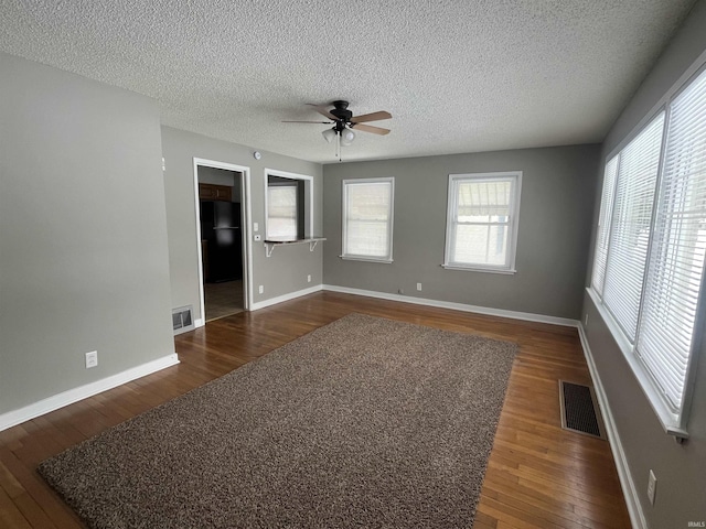 unfurnished room with dark wood-style floors, baseboards, visible vents, and a textured ceiling