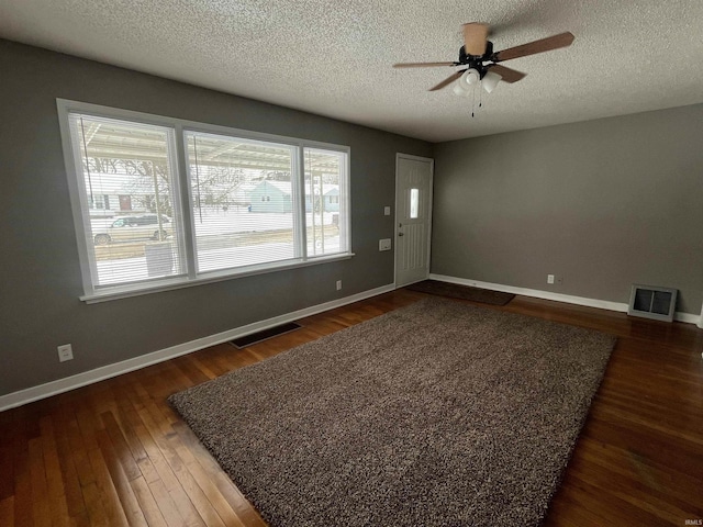 empty room featuring baseboards, visible vents, ceiling fan, and dark wood-style flooring