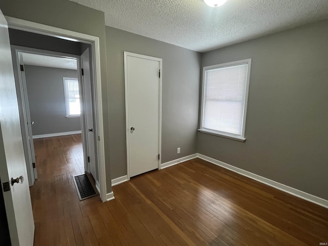 unfurnished bedroom with baseboards, visible vents, dark wood finished floors, and a textured ceiling